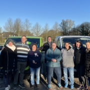 Helferinnen und Helfer mit Pfarrer Müller vor ihrer Abreise vor den abfahrbereiten Bussen